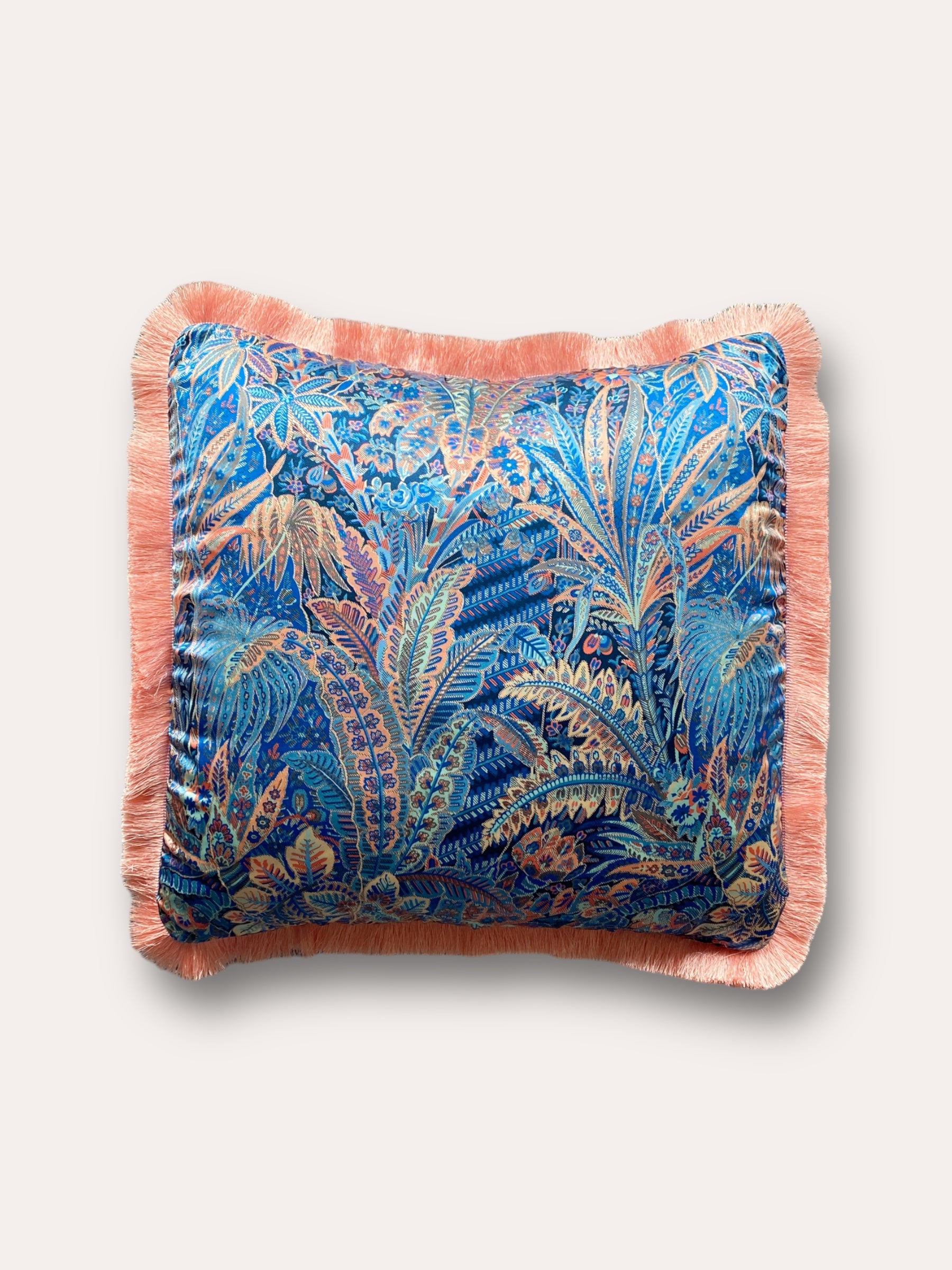 Close-up image of a Liberty Fabric Adelphi Voyage Silk Cushion with a peach fringe edge. The cushion features intricate patterns on luxurious silk fabric, adding a touch of elegance and sophistication to any home decor.