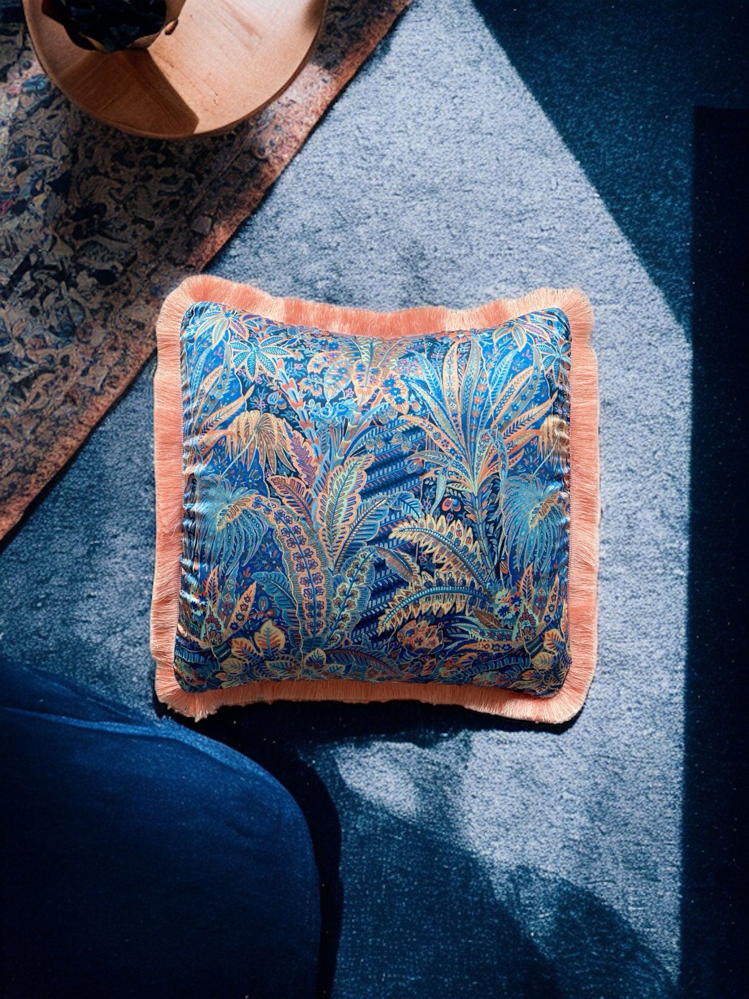 Close-up image of a Liberty Fabric Adelphi Voyage Silk Cushion with a peach fringe edge. The cushion features intricate patterns on luxurious silk fabric, adding a touch of elegance and sophistication to any home decor.