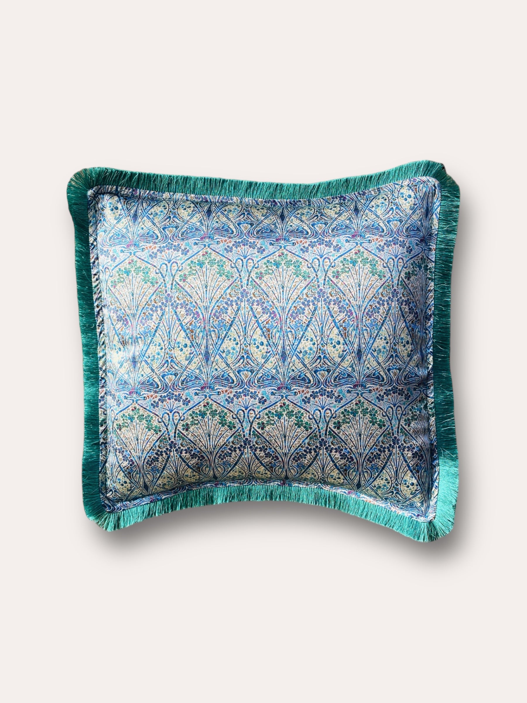 Close-up image of a Liberty Fabric Ianthe Blossom Silk Cushion with a pine green fringe edge. The cushion showcases intricate floral patterns inspired by Ianthe Blossom design on luxurious silk fabric, adding elegance and charm to any home decor.