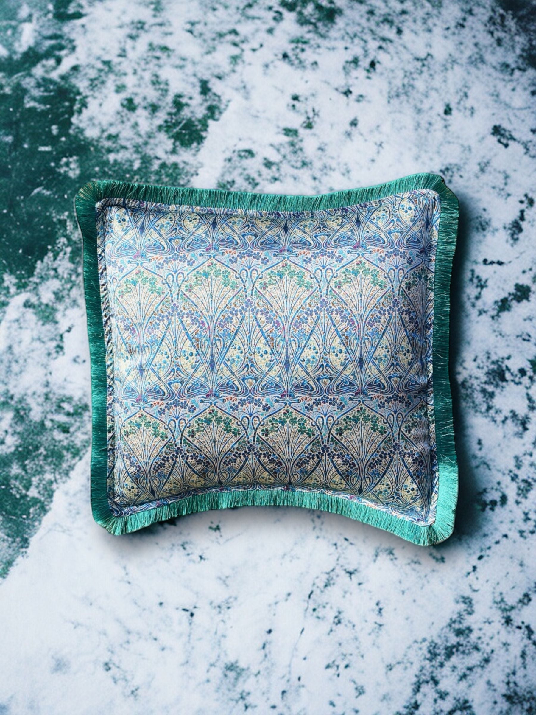 Close-up image of a Liberty Fabric Ianthe Blossom Silk Cushion with a pine green fringe edge. The cushion showcases intricate floral patterns inspired by Ianthe Blossom design on luxurious silk fabric, adding elegance and charm to any home decor.