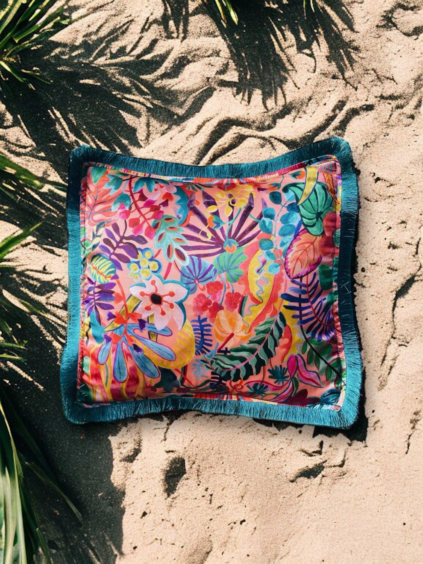 Close-up image of a Liberty Fabric Jungle Trip Silk Cushion with a teal green fringe edge. The cushion features intricate jungle-inspired patterns on luxurious silk fabric, adding vibrancy and sophistication to any home decor.