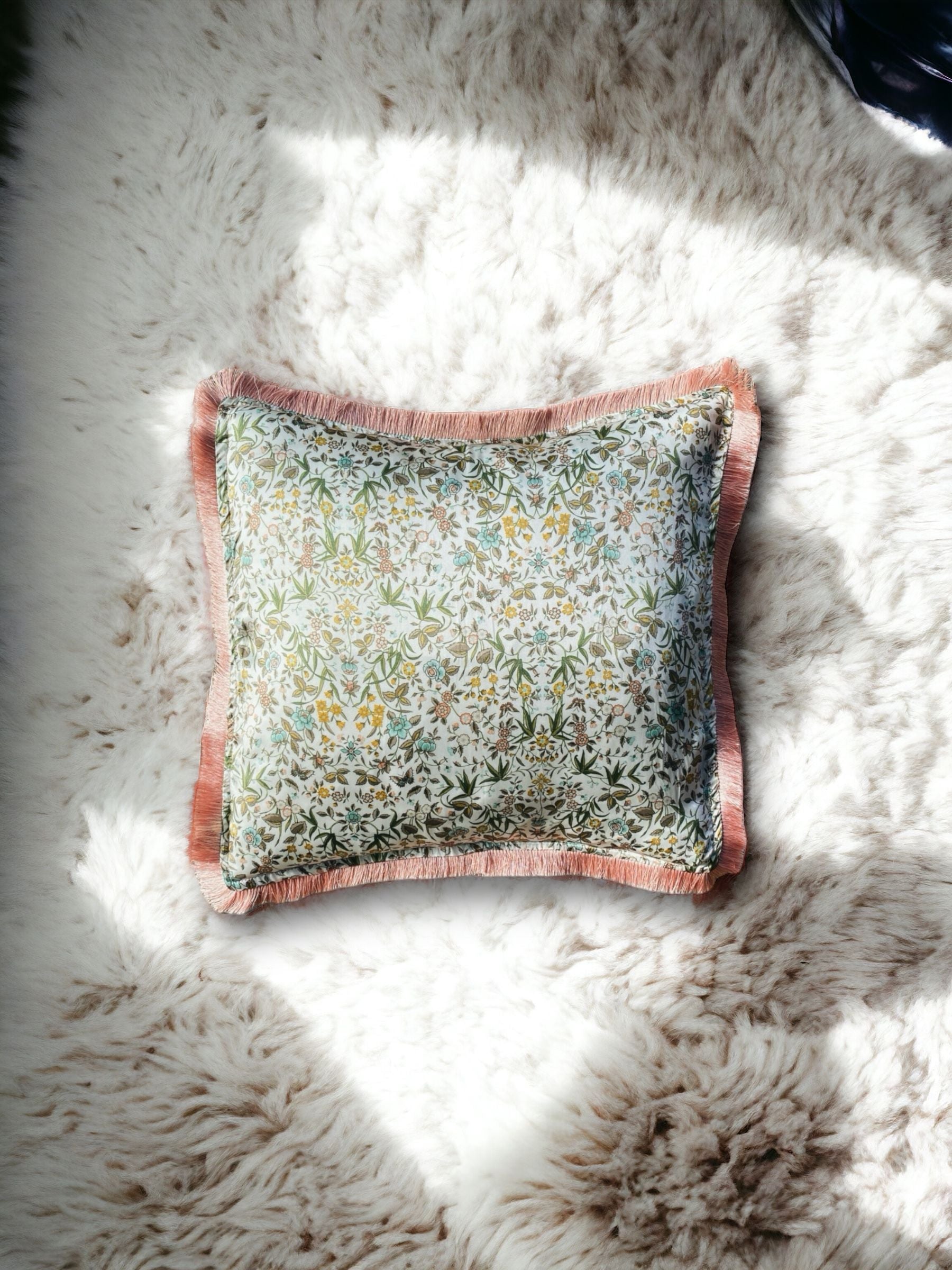 Close-up image of a Liberty Fabric Tapestry Silk Cushion with a delicate dusty pink fringe edge. The cushion features an intricate tapestry design crafted from sumptuous silk, adding sophistication and warmth to any home decor.